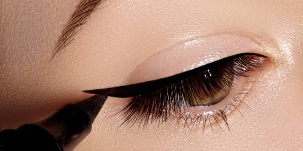 Close-up photo of female eyes. Woman appling black eye liner. Fashion makeup with perfect arrows shape. Retro style and chic evening make-up. Cosmetics and make up