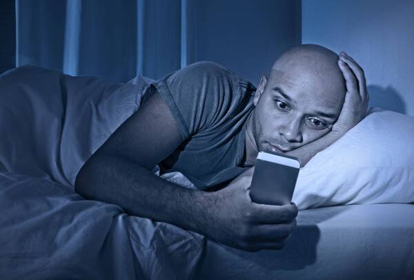 young cell phone addict man awake at night in bed using smartphone